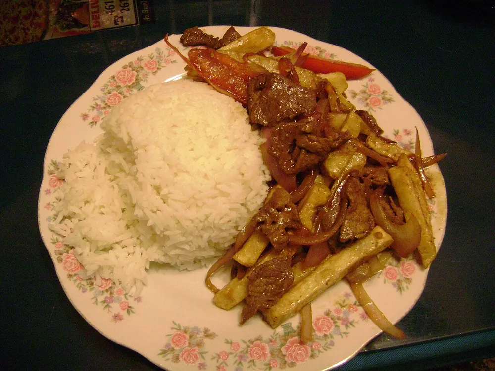 Lomo saltado on a plate with white rice — beef, red onion and chips tossed together