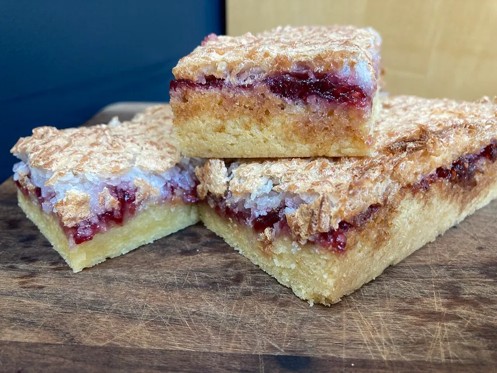 Three squares of Louise cake showing all three layers — biscuit base, raspberry jam and coconut meringue