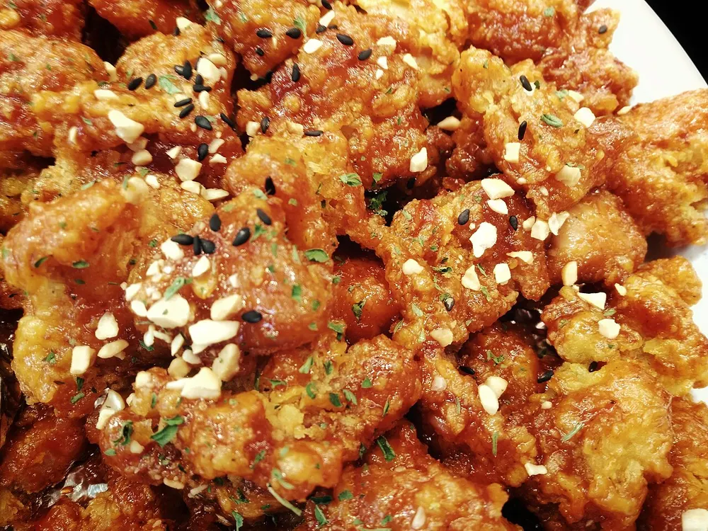 Dakgangjeong — crisp fried chicken in a glossy red glaze, scattered with chopped peanuts and sesame seeds
