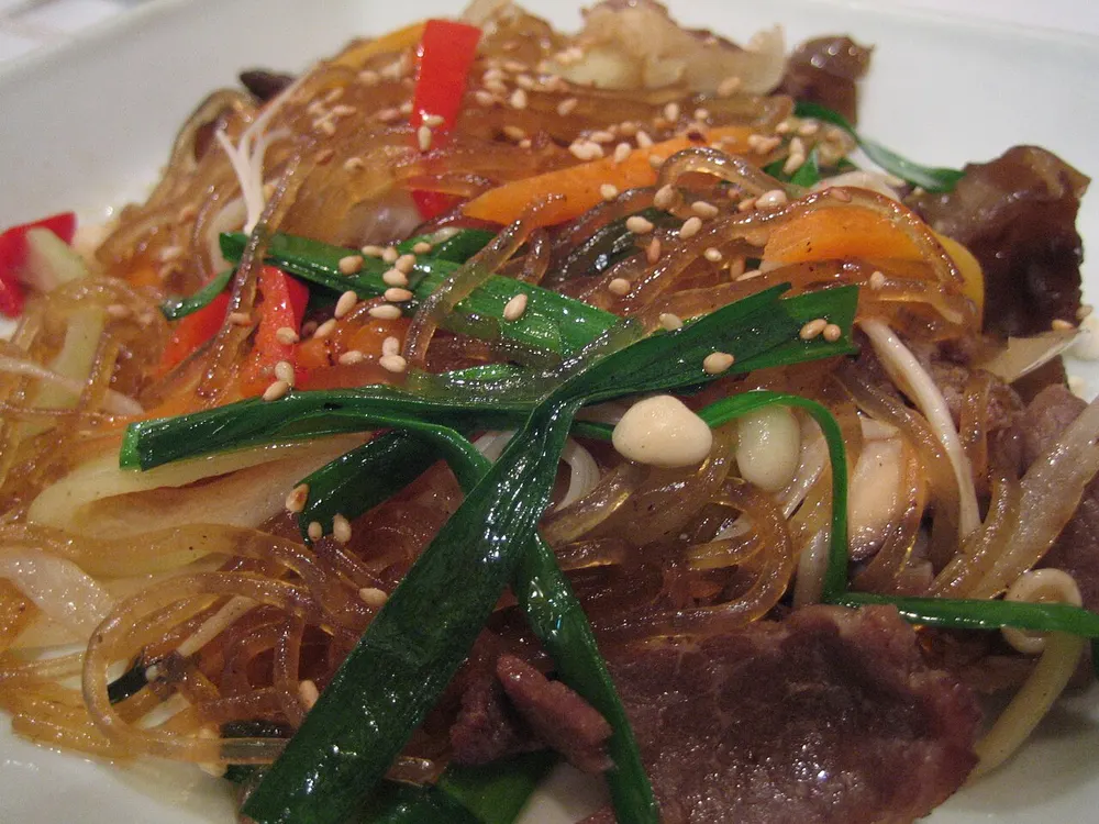 Japchae — glass noodles tossed with beef, onion, green onion and red pepper, scattered with sesame seeds