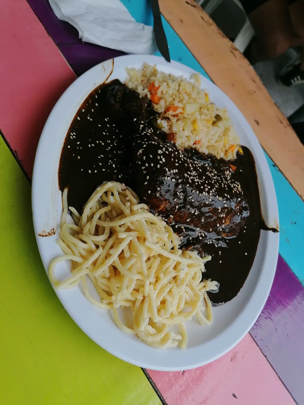Chicken covered in dark glossy mole poblano sprinkled with sesame seeds, served with rice