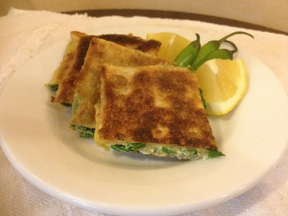 Squares of fried mutabbaq cut open, the green leek and meat filling showing, with lemon and chillies