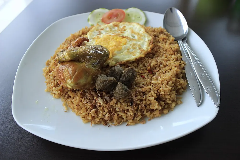 A plate of Indonesian fried rice topped with a fried egg, with cucumber and tomato slices