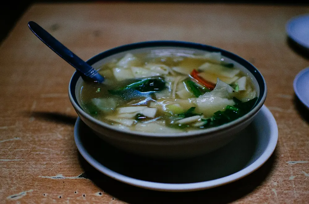 A bowl of thukpa — flat hand-torn noodles with cabbage and greens in a clear broth