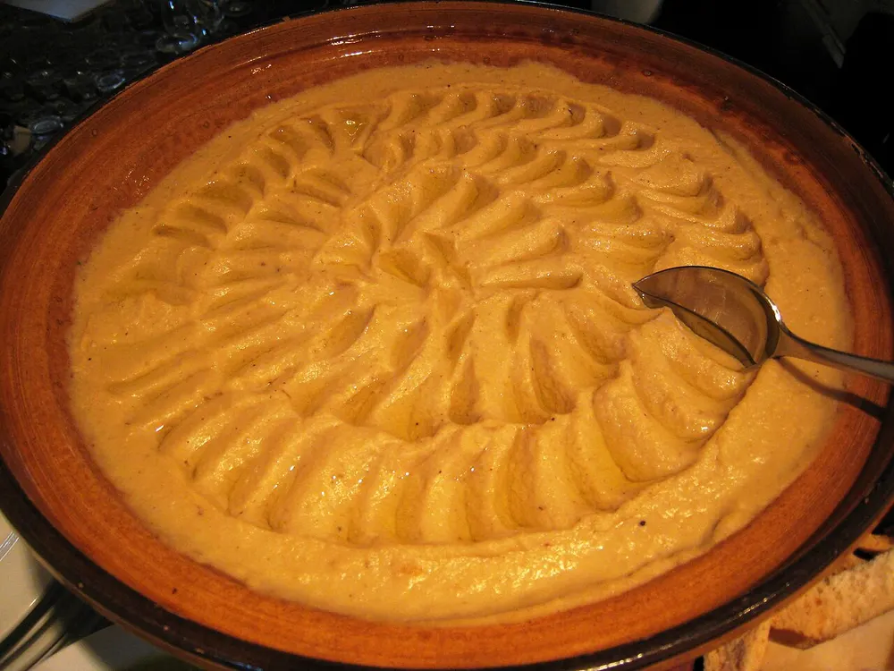 A wide bowl of smooth hummus, swirled with the back of a spoon and glossy with olive oil