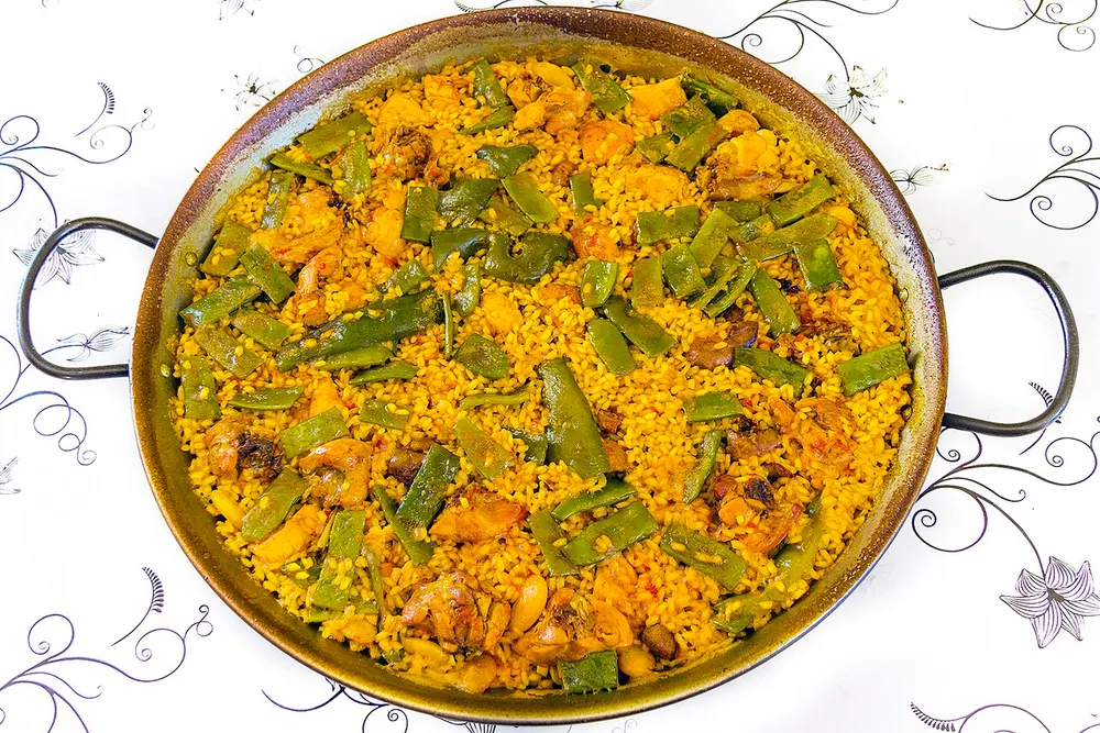 A wide paella pan of saffron rice with chicken, flat green beans and butter beans