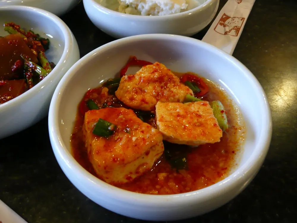 A bowl of dubu-jorim: tofu slices in a red chili-soy sauce with scallion