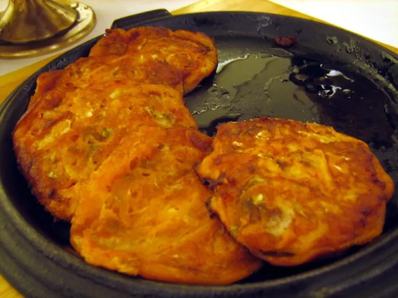 Golden-red kimchi pancakes frying in a black pan
