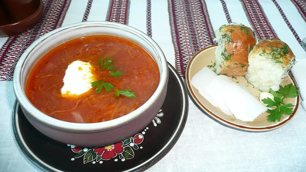 Borscht with smetana beside a plate of pampushky and slices of salo