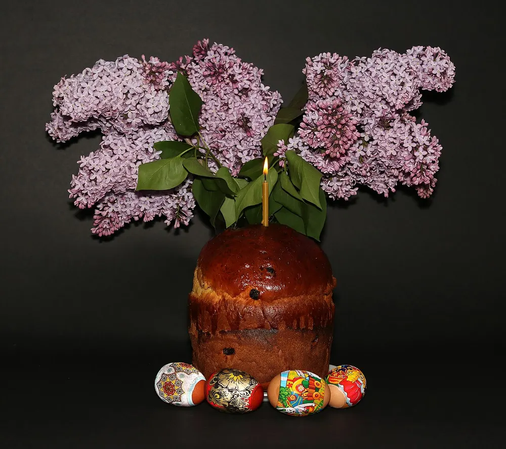 A tall glazed paska with painted Easter eggs at its base and a lit candle on top
