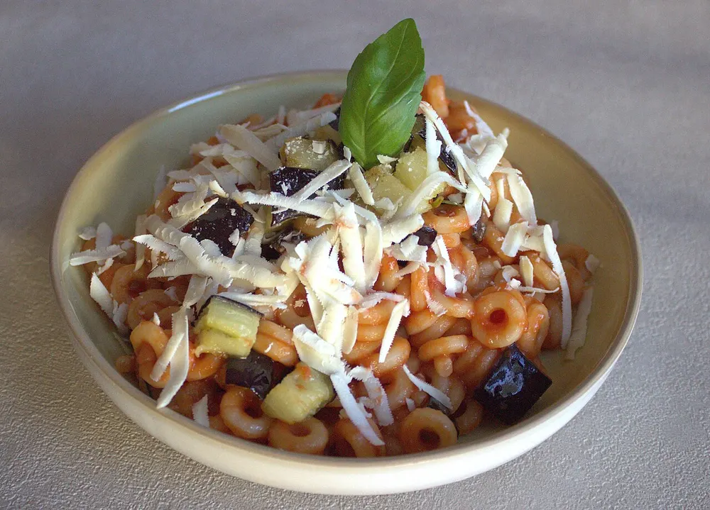 A bowl of pasta alla Norma topped with shaved ricotta salata and a basil leaf