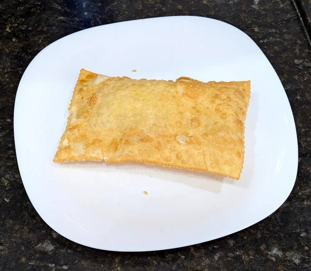 A single deep-fried pastel on a white plate — a pale golden rectangle covered in blisters, its edges crimped shut with a fork