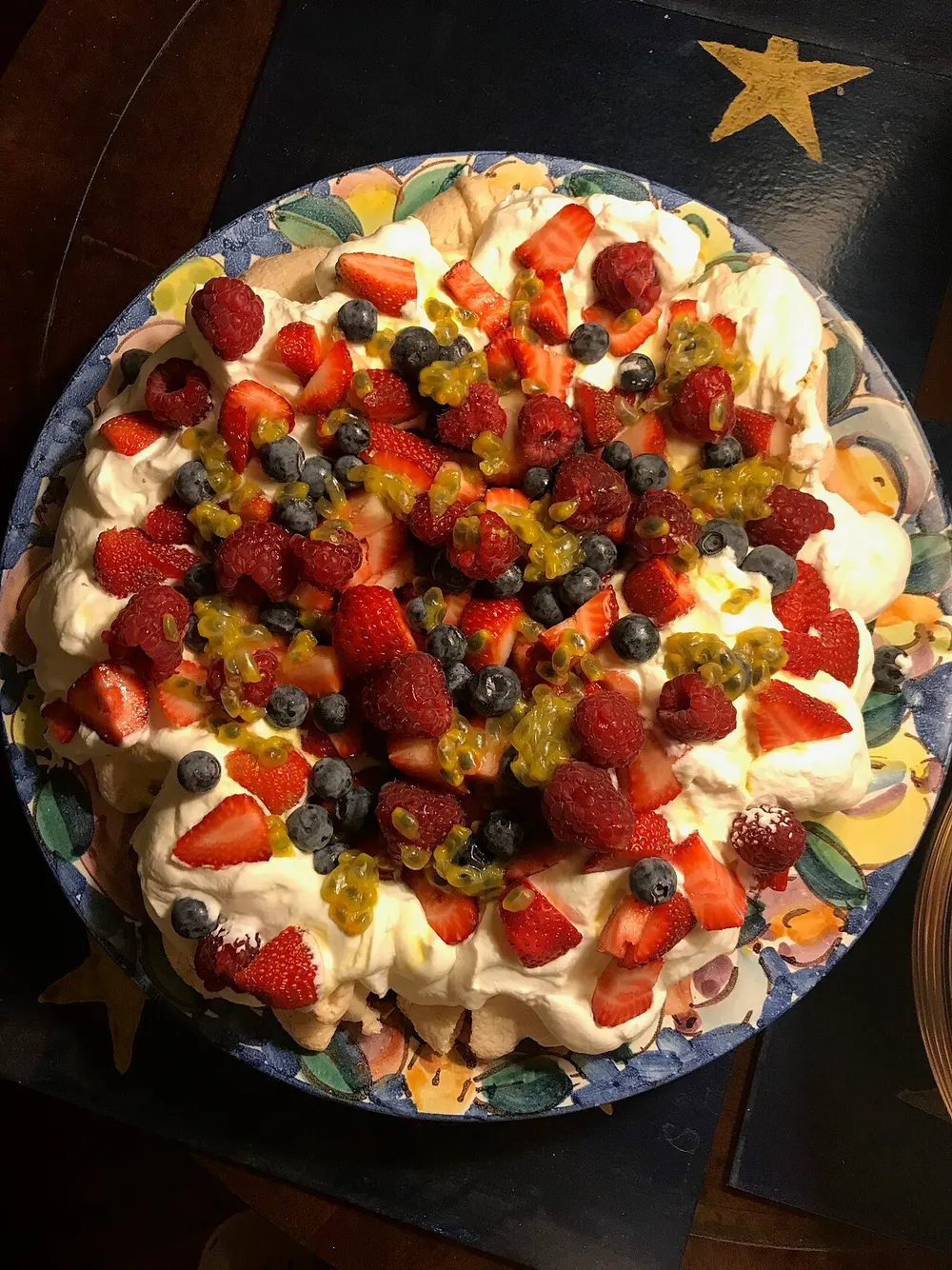 A pavlova under whipped cream, strawberries, raspberries, blueberries and passionfruit