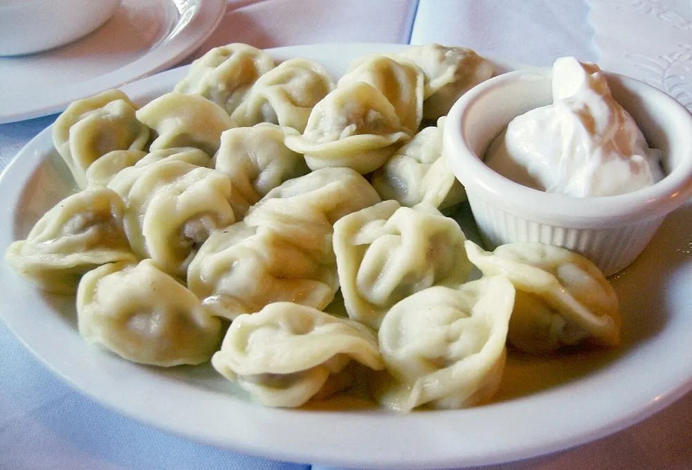 A plate of small boiled pelmeni dumplings with a dish of sour cream