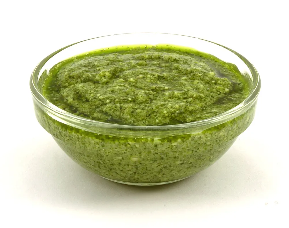A glass bowl of bright green basil pesto