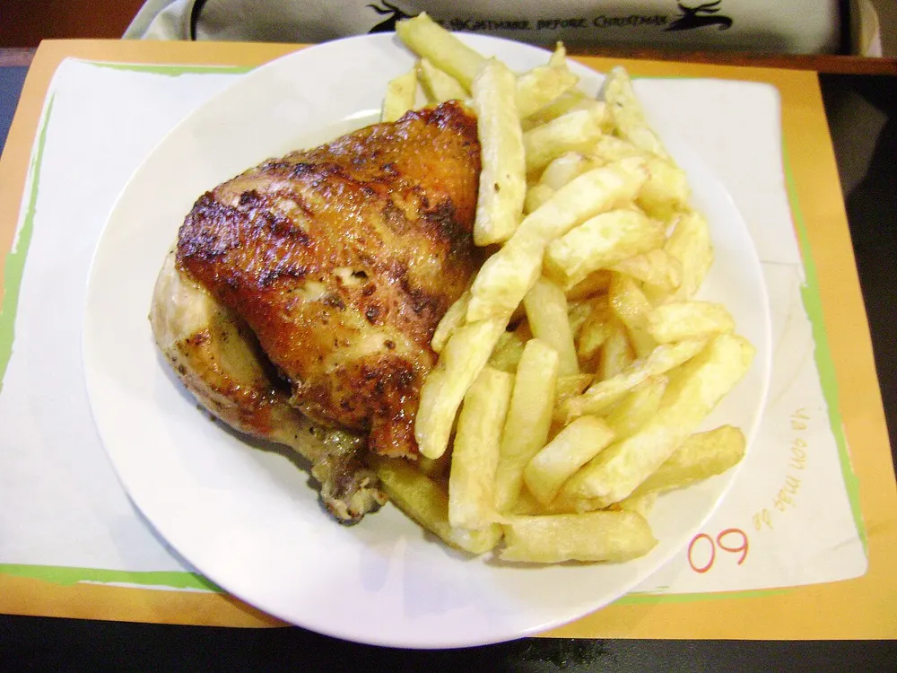 A quarter of pollo a la brasa with chips, the skin dark from the marinade