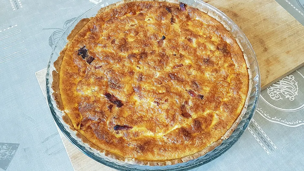 A quiche Lorraine baked golden in a glass dish, pieces of bacon showing through the custard