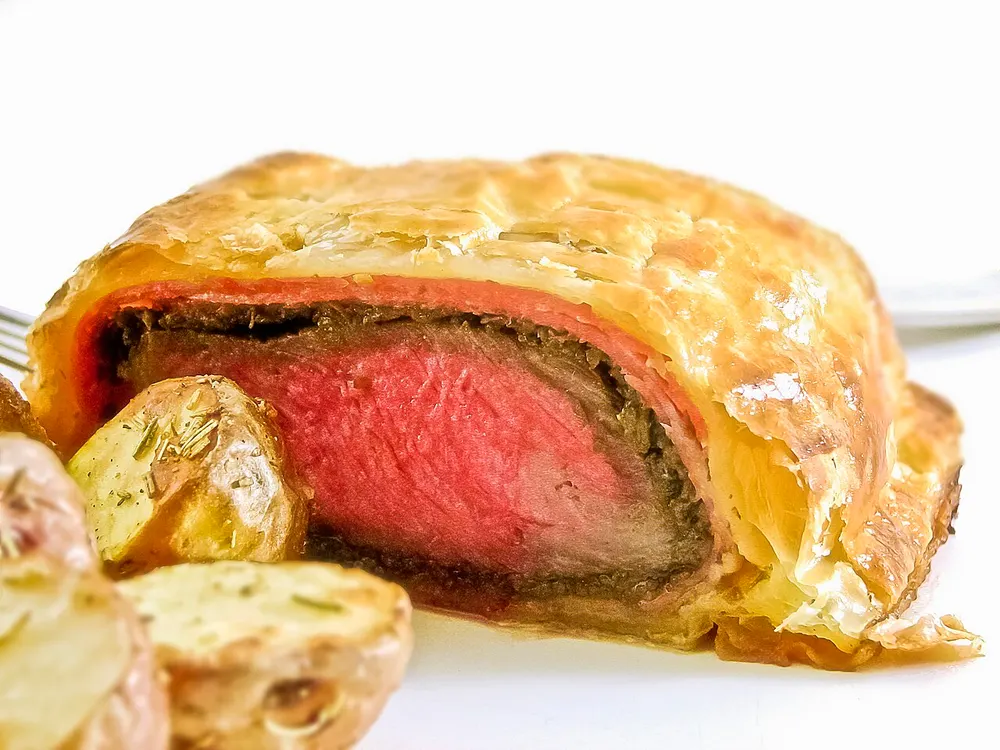 A beef Wellington cut open, showing rare pink beef inside mushroom duxelles and golden puff pastry