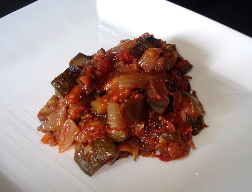 A plate of ratatouille — cubes of eggplant and zucchini with onion in a glossy tomato stew