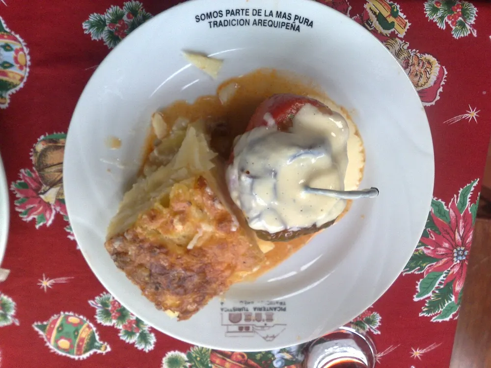 Rocoto relleno with a cheese sauce over it, served with a slice of pastel de papa