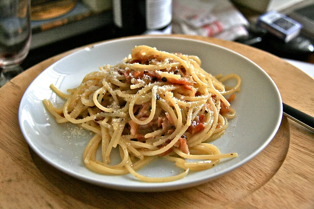 A plate of spaghetti carbonara with bacon, melted cheese and black pepper