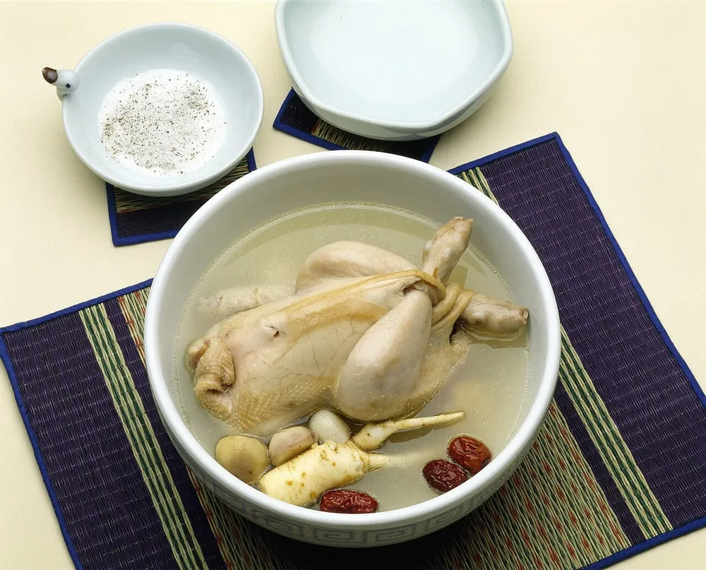A stone bowl of samgyetang with a whole stuffed chicken in milky broth