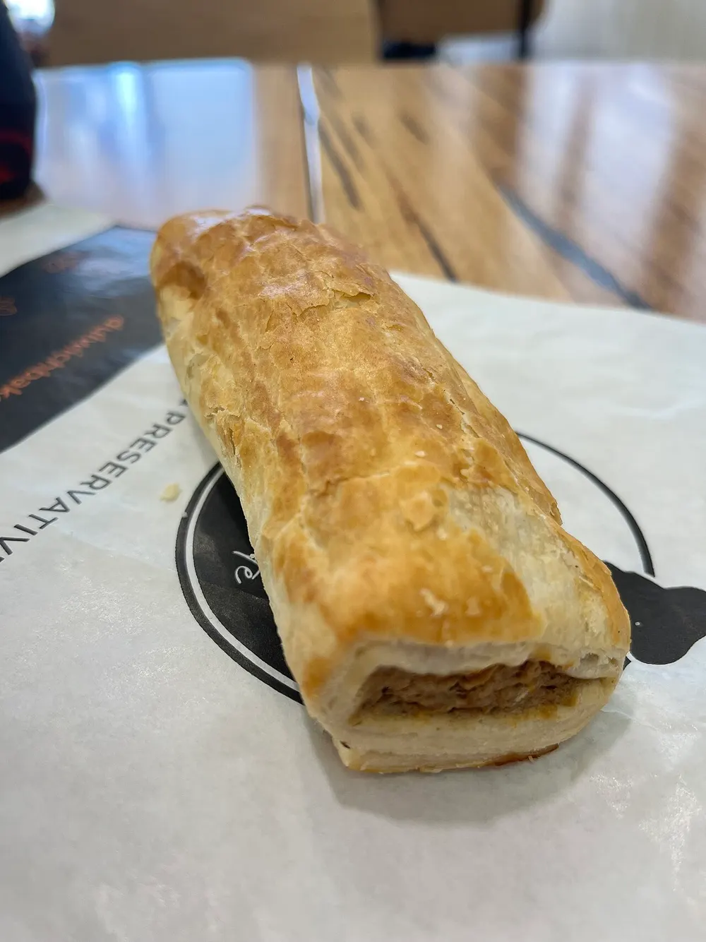 A golden puff-pastry sausage roll with the meat filling visible at the cut end