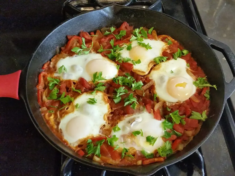 A skillet of shakshuka — eggs poached in a tomato and red pepper sauce, scattered with parsley