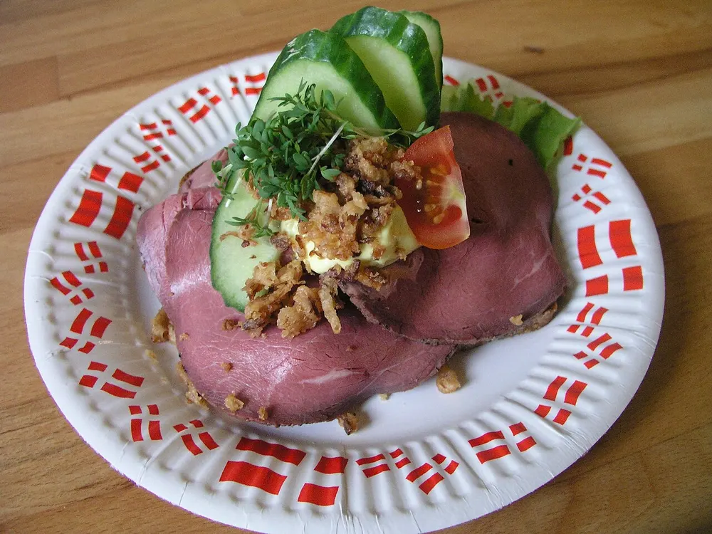 A smørrebrød of roast beef with remoulade, crispy onion and cucumber, on a Danish flag plate