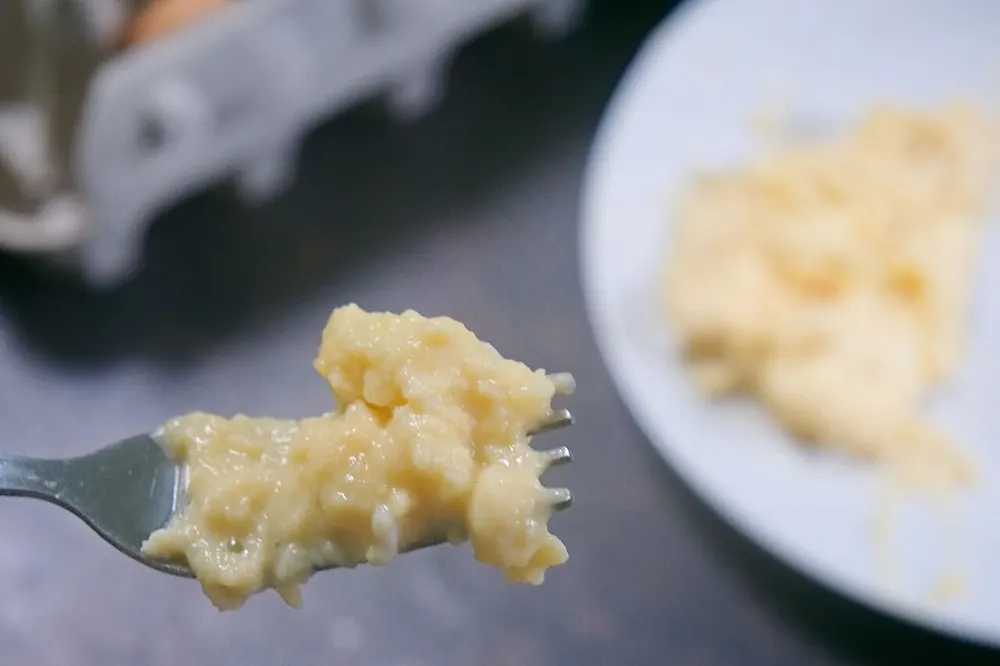 A forkful of pale, glossy scrambled egg in small soft curds