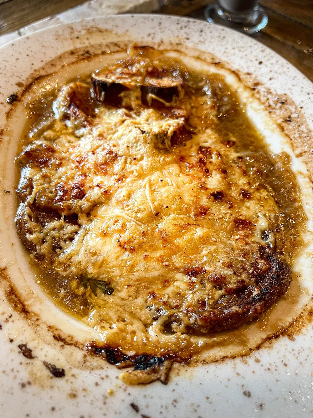 Onion soup under a browned, blistered cheese crust that runs to the rim of the dish