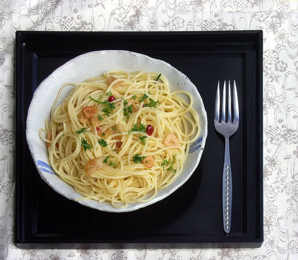 A bowl of glossy spaghetti tossed with golden garlic slices, red chili and parsley