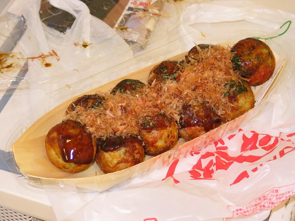 A boat of takoyaki topped with sauce and bonito flakes