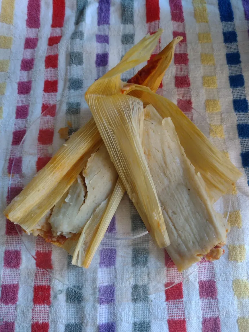 Opened tamales in dried corn husks showing pale masa with red sauce filling inside