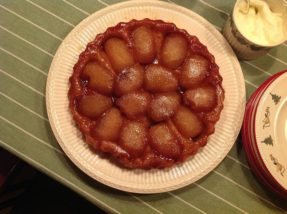 A tarte Tatin turned out on a plate, halved apples arranged in a ring and dark with caramel