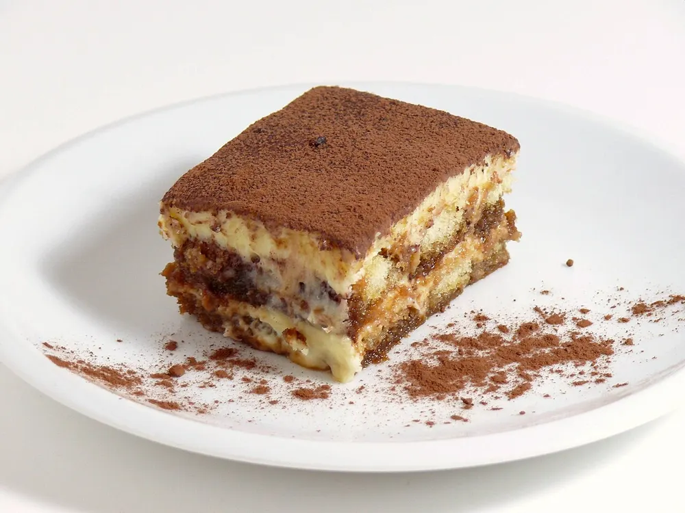 A portion of tiramisù dusted with cocoa, showing the layers of sponge and cream