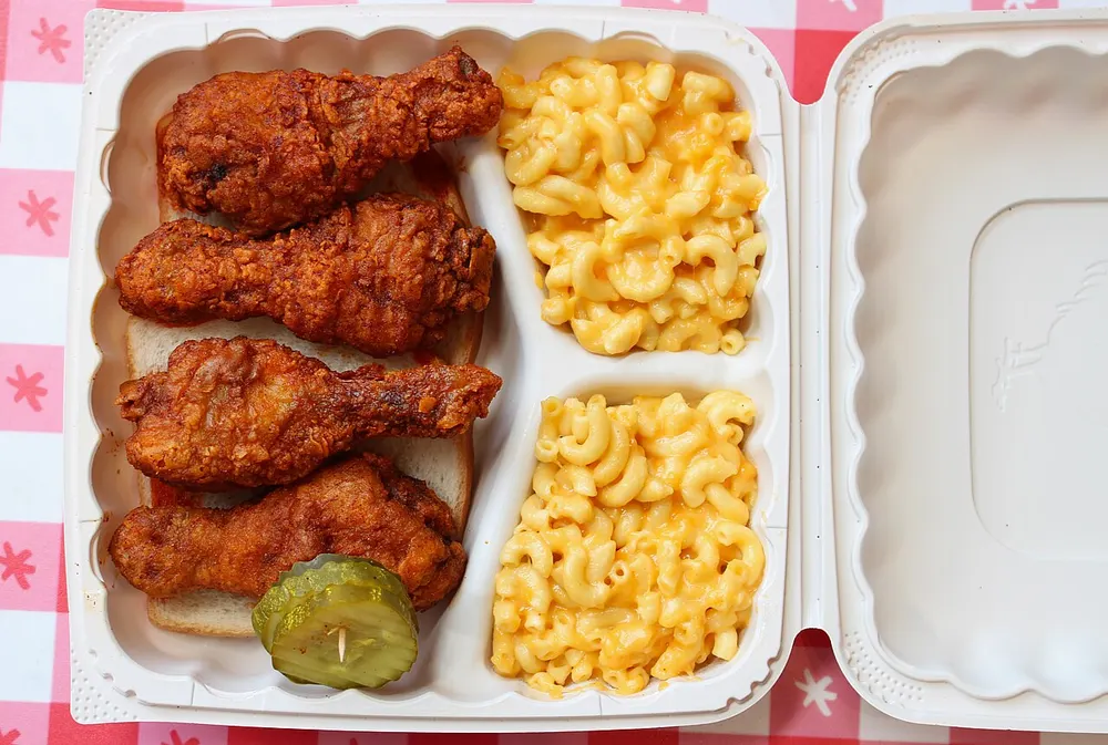 Red-glazed Nashville hot chicken pieces served on white bread with dill pickle slices