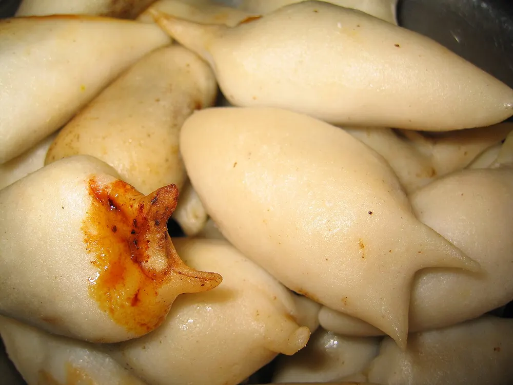 Steamed yomari, pinched into tapered fig shapes, one broken open to show the dark molasses filling
